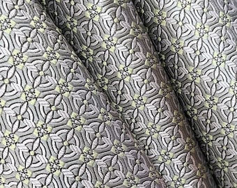 May include: Close-up of a fabric with a repeating pattern of small green and silver circles and squares. The fabric is folded in a way that creates a diagonal line.