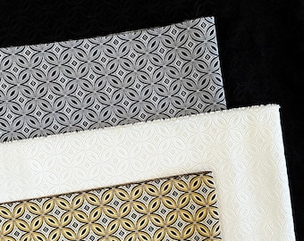 May include: Three fabric swatches with a geometric pattern. The top swatch is black, the middle swatch is gray with a silver pattern, and the bottom swatch is white with a gold pattern.