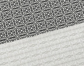 May include: A black and white patterned fabric with a repeating geometric design. The fabric is folded in half, revealing a silver patterned fabric underneath.