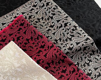 May include: Four different fabric swatches with paisley patterns. The swatches are in black, silver, red, and cream.