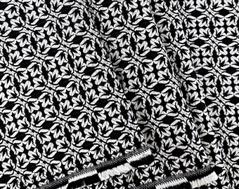 May include: Black and white fabric with a repeating geometric pattern. The fabric has a fringed edge.