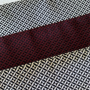 Puede incluir: Primer plano de una tela con un patrón geométrico. La tela es negra, blanca y burdeos. El patrón está formado por pequeños triángulos.