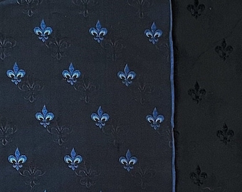 May include: A dark blue fabric with a repeating pattern of blue fleur-de-lis. The fabric has a subtle sheen and a textured surface.