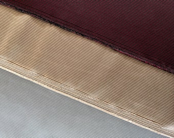 May include: Close-up of three fabric swatches. The top swatch is a dark red corduroy, the middle swatch is a light brown corduroy, and the bottom swatch is a light gray fabric.