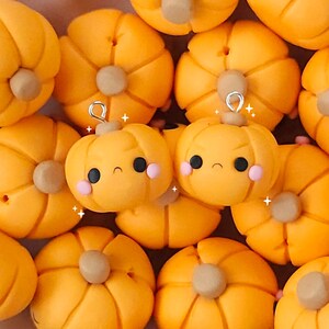Puede incluir: Una colección de adornos de arcilla naranja y amarilla con forma de calabazas con caras de dibujos animados. Las calabazas tienen ojos negros, una boca negra y mejillas rosadas.
