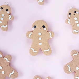 May include: Six gingerbread people ornaments with white icing details and black eyes. The gingerbread people are on a pink background.