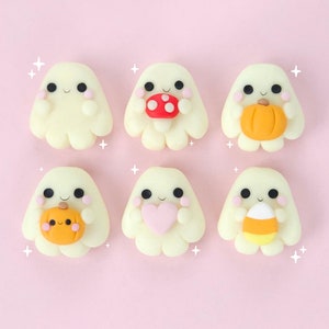 Puede incluir: Seis adornos blancos en forma de fantasma con diferentes decoraciones de temática de Halloween. Los fantasmas sostienen una calabaza, un corazón, un caramelo de maíz, un hongo y una calabaza con una cara.