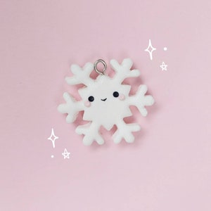 May include: A white snowflake charm with a cute cartoon face. The snowflake has a silver loop for hanging.