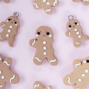 May include: A set of six gingerbread man ornaments with white icing details. The gingerbread men have different expressions, including angry, sad, and surprised. The ornaments are perfect for adding a festive touch to your Christmas tree or home decor.