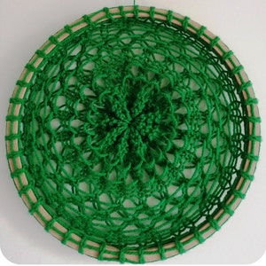 Puede incluir: Un mandala de ganchillo verde con un marco de aro de madera. El mandala tiene un diseño circular con detalles intrincados.