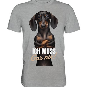 May include: A gray t-shirt with a black and brown dachshund dog with its arms crossed. The dog is looking directly at the viewer. The text "ICH MUSS Gar nix!" is printed on the shirt.