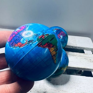 Puede incluir: Tres pelotas anti estrés azules y blancas con un mapa del mundo impreso en ellas. Las pelotas están sobre una superficie de madera blanca.