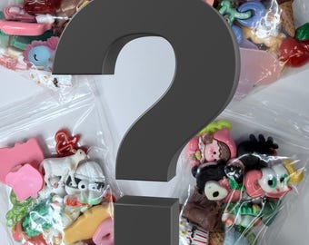 May include: Assorted colorful resin charms in clear plastic bags. The charms include various shapes like bows, flowers, animals, and food items. The image is partially obscured by a large gray question mark.