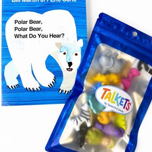 May include: A board book titled Polar Bear, Polar Bear, What Do You Hear? by Bill Martin Jr and Eric Carle, featuring a white polar bear illustration on a blue background, next to a blue resealable pouch containing assorted small animal figures.