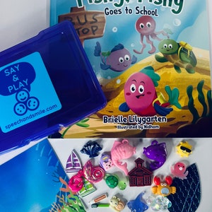May include: A blue plastic container with a lid, a book titled "Fishy, Fishy Goes to School" by Brielle Lilygarten, illustrated by Nidhom, and a variety of colorful plastic toys, including a school bus, a turtle, a fish, a crab, a seashell, a starfish, a sailboat, and a toothbrush. The toys are on a white surface.