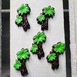 Pode incluir: Cinco botões em forma de palmeira verde e marrom. Os botões são feitos de resina e têm um acabamento brilhante.