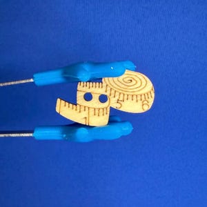 Peut inclure: Une règle de couture en bois et un mètre ruban en bois avec un motif circulaire sont maintenus par des outils bleus sur fond bleu. Les mesures sont en centimètres.