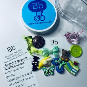 May include: A clear plastic jar with a blue lid that says "Bb speechandsmile.com" on it. The jar contains a variety of small toys, including a butterfly, a bat, a book, a banana, a boot, a bird, a bike, a bear, a ball, and a button. A white card with the letter "Bb" and instructions for making the "B" sound is also included.