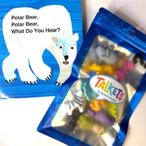 Op de afbeelding: Een kartonboek getiteld Polar Bear, Polar Bear, What Do You Hear? door Bill Martin Jr en Eric Carle, met een illustratie van een witte ijsbeer op een blauwe achtergrond, naast een blauw hersluitbaar zakje met kleurrijke dierenfiguren.