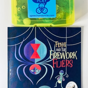 Może przedstawiać: Niebieski i żółty plastikowy pojemnik z naklejką z napisem "SAY & PLAY" i stroną internetową "speechandsmile.com". Pojemnik zawiera zielonego plastikowego owada, żółtą piłkę i zielony materiał przypominający tiul. Książka zatytułowana "Fenix i Lotnicy Od Fajerwerków" z kolorową ilustracją pająka i muchy na okładce. Książka jest częścią serii "Once Upon a Dance" i jest opisana jako "Taniec-Wymyśl-Ruchowa Historia Kreatywna".