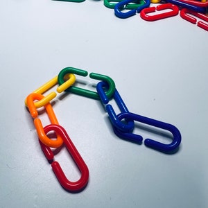 May include: A chain made of colorful plastic links. The links are in the colors of the rainbow, starting with red and ending with blue. The chain is arranged in a curved shape.