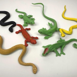 May include: A selection of toy reptiles in various colours. The toys include snakes and lizards in black, green, yellow, and red. The plastic toys are arranged on a white surface.