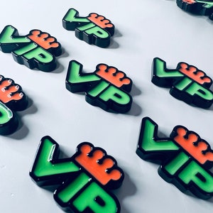 Può includere: Più badge VIP verdi e neri con una corona arancione in cima. I badge sono disposti in fila su una superficie bianca.