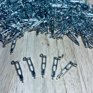 Puede incluir: Cinco abalorios de metal plateado en forma de muletas sobre una superficie de madera. Los abalorios son pequeños y detallados, con un bucle en la parte superior para sujetarlos a un collar o pulsera.