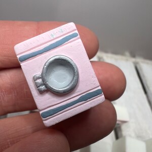 May include: A miniature pink book with a silver handle and gray stripes. The book is made of ceramic and is a decorative item.