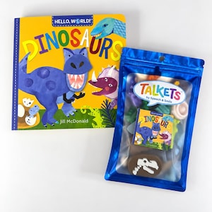 May include: A Hello, World! Dinosaurs book by Jill McDonald featuring a blue T-Rex on a yellow cover, alongside a blue Talkets by Speech & Smile pouch containing small dinosaur-themed items and a miniature replica of the book cover.