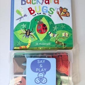 May include: A children's book titled "Backyard Bugs" with insect illustrations, and a clear plastic container with toy insects and a "Say & Play" sticker.