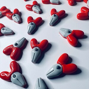 May include: A collection of red and gray decorative objects, each with a three-petal design. The objects have a glossy finish and are arranged on a white surface. The red petals are rounded, and the gray center has a pointed shape.