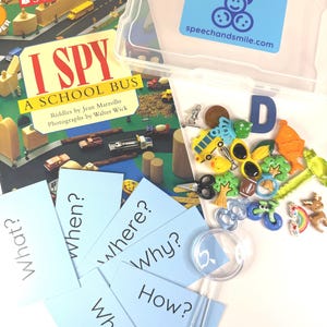 May include: A children's educational game set including an "I Spy" book about a school bus, question cards, and small toys. A clear plastic container with a "Say & Play" sticker is also visible. The set is designed for learning and play.