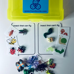 Könnte beinhalten: Eine gelbe Kunststoff-Aufbewahrungsbox mit einem blauen Etikett mit der Aufschrift "SAY & PLAY" und "speechandsmile.com". Darunter Karten mit der Aufschrift "Insekt, das fliegen kann" und "Insekt, das nicht fliegen kann" mit Insektenillustrationen und Spielzeug-Insekten aus Kunststoff.