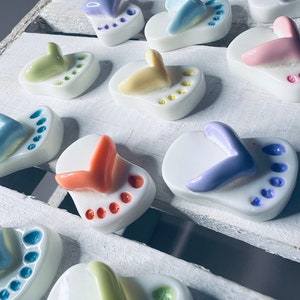 Könnte beinhalten: Eine Sammlung von Keramik-Flip-Flop-Anhängern in verschiedenen Farben, darunter Pink, Blau, Gelb, Grün und Lila. Jeder Flip-Flop hat eine weiße Basis und ein buntes Design auf der Oberseite.