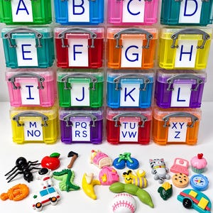 Könnte beinhalten: Ein Set aus sechzehn bunten, durchscheinenden Kunststoff-Aufbewahrungsboxen mit grauen Griffen, die jeweils mit Buchstaben von A bis Z beschriftet sind. Unter den Boxen befinden sich verschiedene kleine Kunststoff-Miniaturfiguren, darunter eine Ameise, Obst, Fahrzeuge und Tiere.
