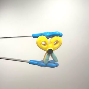 Può includere: Strumento ortodontico giallo e blu con design a forbice. Lo strumento ha un centro giallo a forma di cuore con un punto nero e manici blu. Lo strumento è progettato per le procedure dentali.