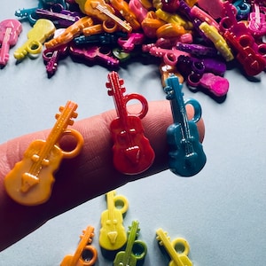 May include: A collection of colorful plastic toy violins. The violins are in various colors, including red, blue, yellow, orange, and green. The violins are arranged in a pile, with some of them lying on a finger.
