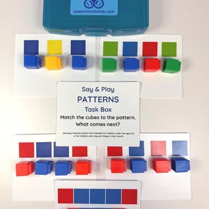May include: A teal plastic storage box with a label that says "Say & Play" and "speechandsmile.com". Below the box are white cards with colourful patterns and matching cubes. The text on the card says "Say & Play PATTERNS Task Box".