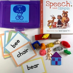 Op de afbeelding: Een logopedieset met een paarse plastic opbergdoos met een Say & Play-label, een boek getiteld Speech made Simple, een stapel woordkaarten met bee, chair en bear, en diverse kleine plastic dieren- en objectfiguurtjes.