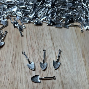 Könnte beinhalten: Vier silberfarbene Miniatur-Schaufeln mit spitzen Spitzen und Griffen. Die Schaufeln sind in einer Reihe auf einer Holzoberfläche angeordnet.