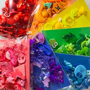 Puede incluir: Bolsas de plástico de colores arcoíris llenas de pequeños juguetes de plástico. Cada bolsa contiene un color diferente de juguetes, incluyendo rojo, rosa, morado, azul, verde, amarillo y naranja.