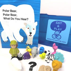 Könnte beinhalten: Ein Kinderbuch mit dem Titel Polar Bear, Polar Bear, What Do You Hear? von Bill Martin Jr und Eric Carle, ein blauer Kunststoff-Aufbewahrungskoffer mit der Aufschrift Say & Play sowie eine Sammlung kleiner Tierfiguren und eine Fragezeichen-Karte.