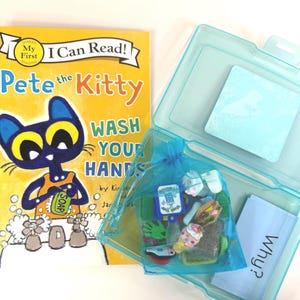 May include: A children's book titled "Pete the Kitty Wash Your Hands" with a blue kitty illustration. A clear plastic case contains a blue drawstring bag filled with small toys and a small blue card with the word "Why?" printed on it.