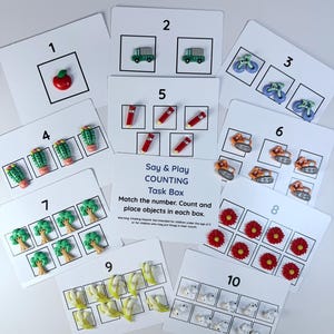 May include: Ten counting task cards, numbered 1 to 10, with matching objects such as apples, buses, and flowers. The cards are designed for early learning and feature the text "Say & Play COUNTING Task Box". The cards are designed for early childhood education.