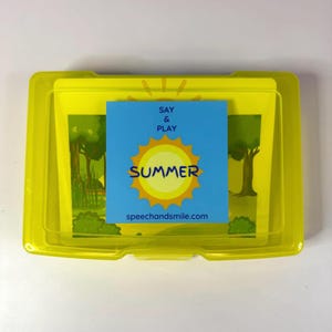 May include: A rectangular yellow plastic storage case containing a set of cards. A blue square label on the front features a yellow sun graphic, the text SAY & PLAY SUMMER, and the website address speechandsmile.com printed in dark blue letters.