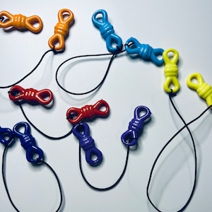 May include: A collection of colorful plastic clasps connected by black string. The clasps are in various colors, including blue, red, yellow, and orange.