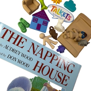 May include: A copy of the book The Napping House by Audrey Wood and Don Wood, accompanied by a collection of small plastic figures including a house, a bed, a chair, a tree, a sun, a cloud, a Talkets logo, and various animal and human figurines.