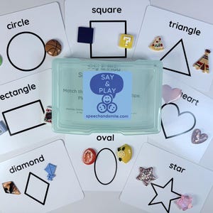 May include: Shape matching cards featuring circle, square, triangle, rectangle, diamond, oval, heart, and star shapes. Each card displays a shape and a corresponding object. A clear plastic case with the text "SAY & PLAY" is in the centre.