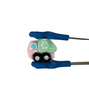 May include: A miniature pink and green recycling truck with black wheels. The truck has a recycling symbol on the back. The truck is held by blue tools against a white background.